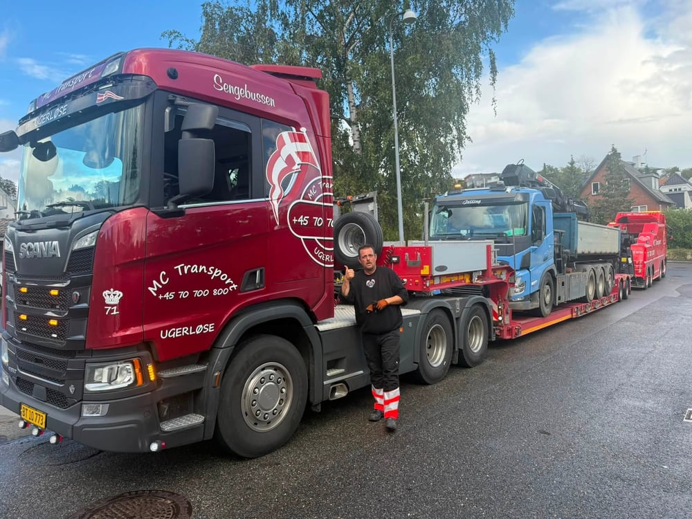 Chauffør hos MC Transport med tommelfinger op ved rød Scania lastbil